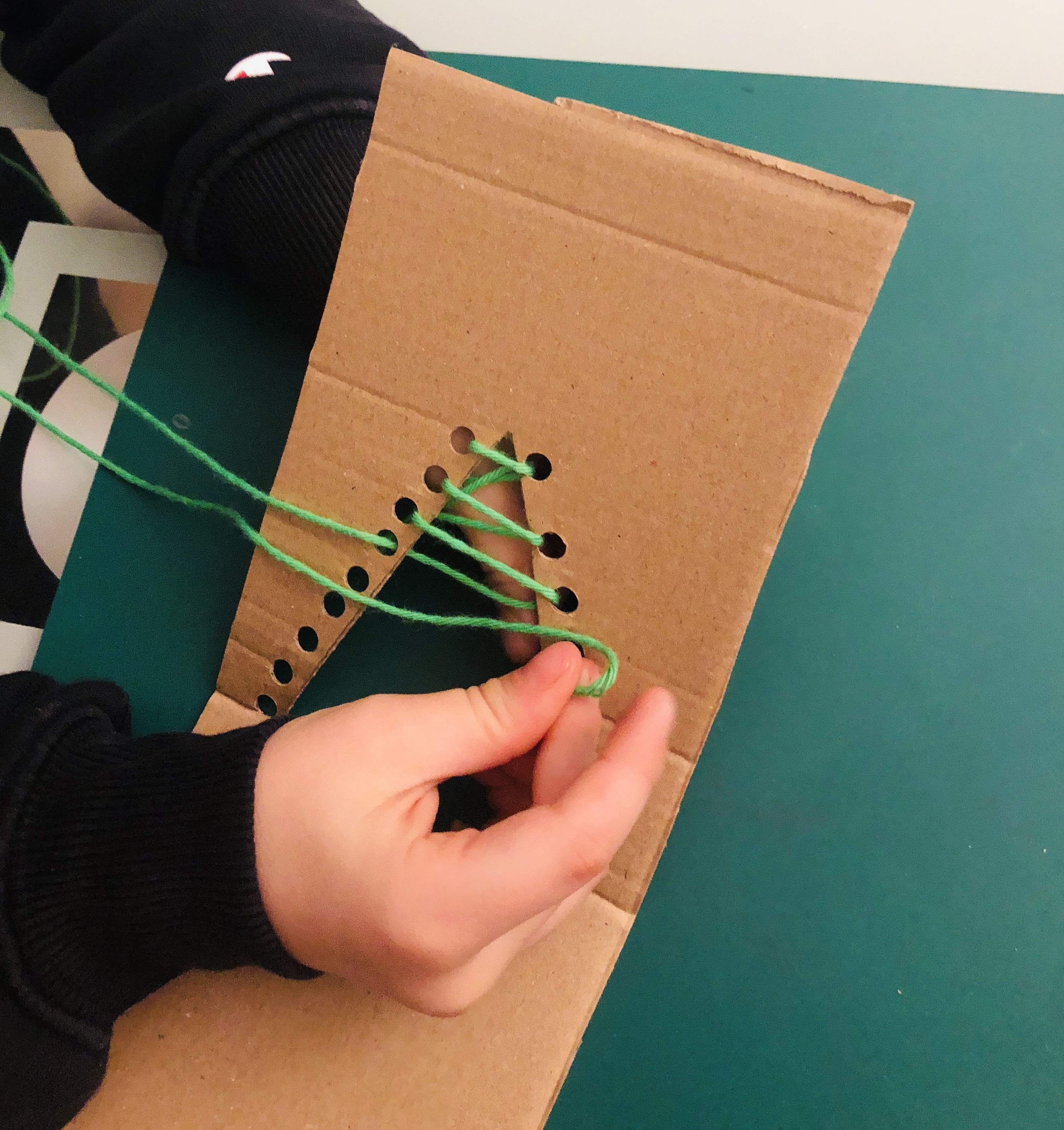 kid pulling thread through holes on a cardboard tree